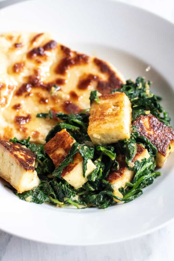 a plate with naan and paneer and spinach.