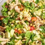grilled chicken green salad with tomatoes, corn, and avocado in a large bowl.