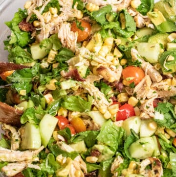 grilled chicken green salad with tomatoes, corn, and avocado in a large bowl.