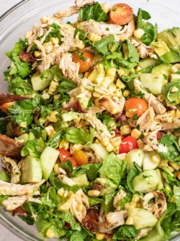grilled chicken green salad with tomatoes, corn, and avocado in a large bowl.