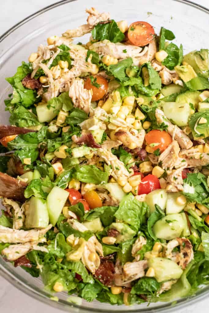 grilled chicken green salad with tomatoes, corn, and avocado in a large bowl