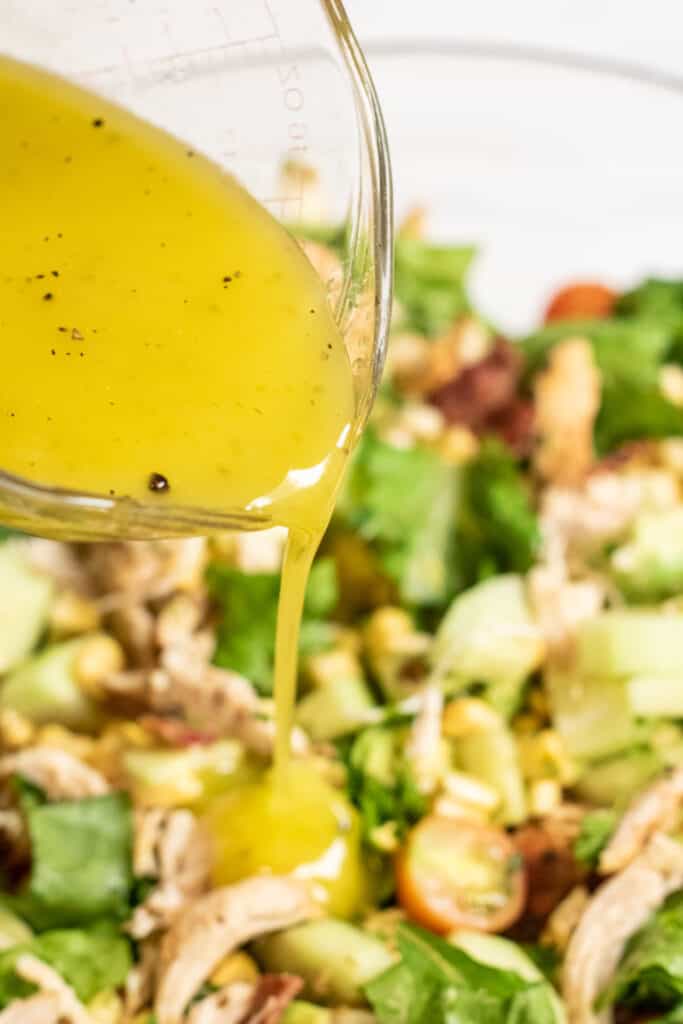 a vinaigrette being poured into a bowl of salad