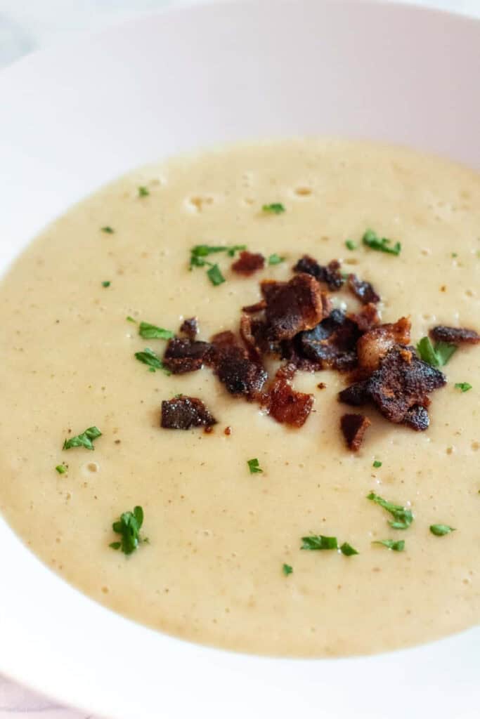 a bowl of creamy soup topped with parsley and crumbled bacon.