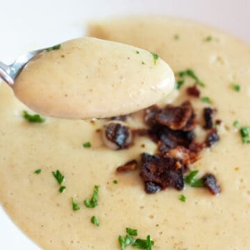 a close up of a spoonful of soup in front of a bowl of soup.