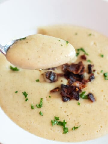 a close up of a spoonful of soup in front of a bowl of soup.