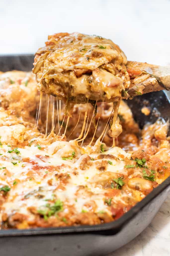 a piece of lasagna coming out of a cast iron skillet with Pinterest pin text.