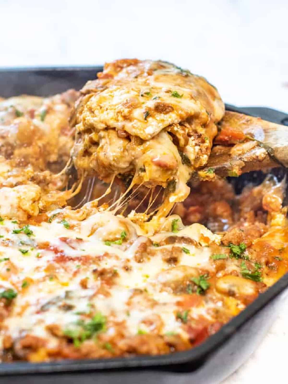 a piece of lasagna coming out of a cast iron skillet with Pinterest pin text.