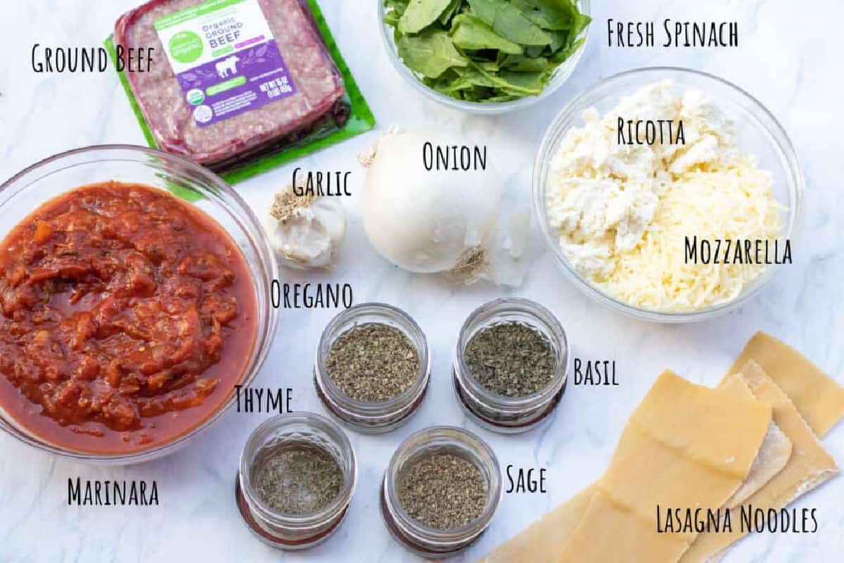ground beef, marinara, cheese, seasoning, lasagna noodles, spinach, and garlic and onion on counter.