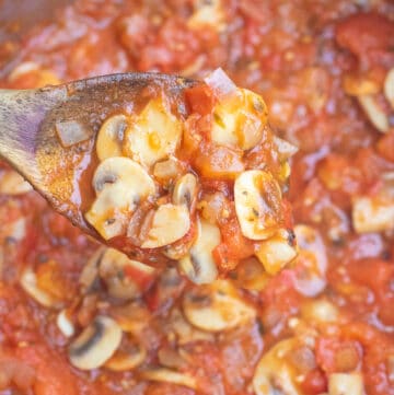 a wooden spoon scooping mushroom marinara in pot.