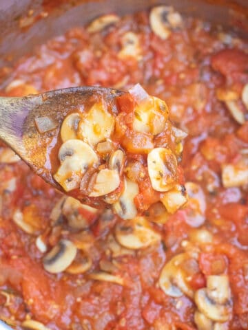 a wooden spoon scooping mushroom marinara in pot.