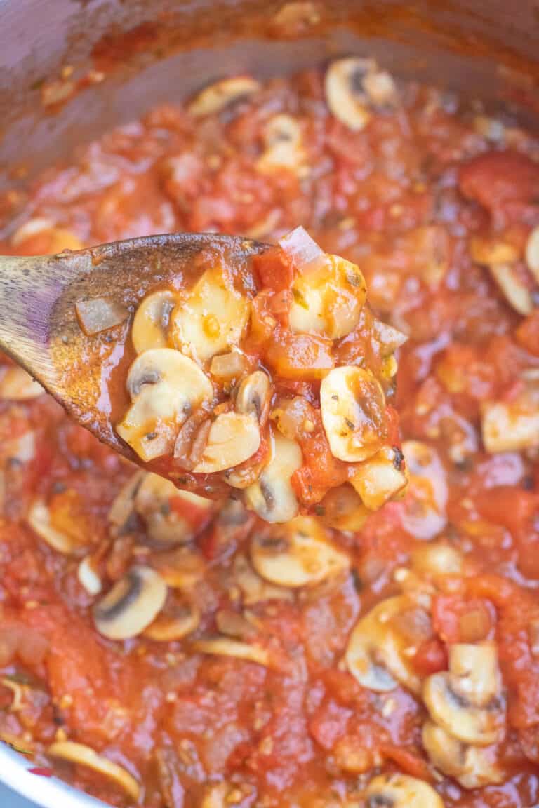 a wooden spoon scooping mushroom marinara in pot.