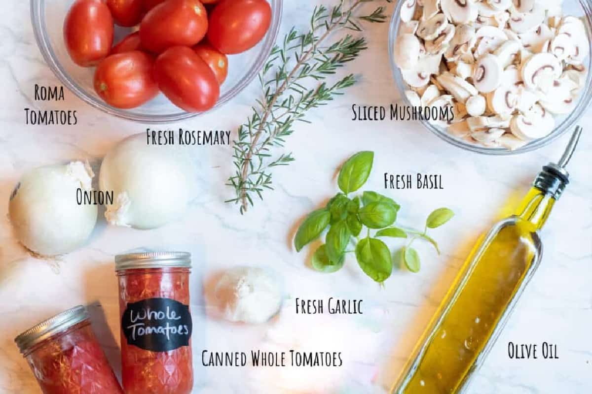 romas, canned tomatoes, olive oil, mushrooms, basil, onions, and rosemary on counter.