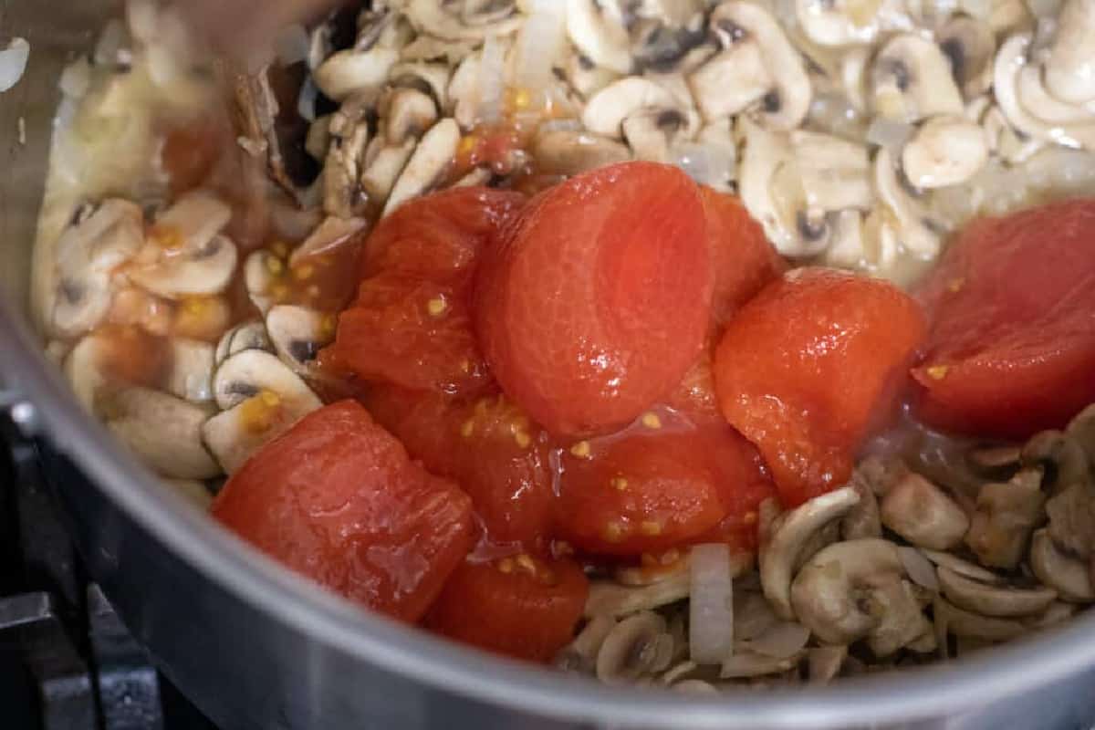whole tomatoes added to cooked mushrooms in a pan.