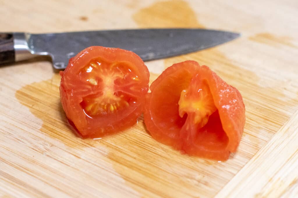 a roma tomato sliced in half on cutting board and one side deseeded