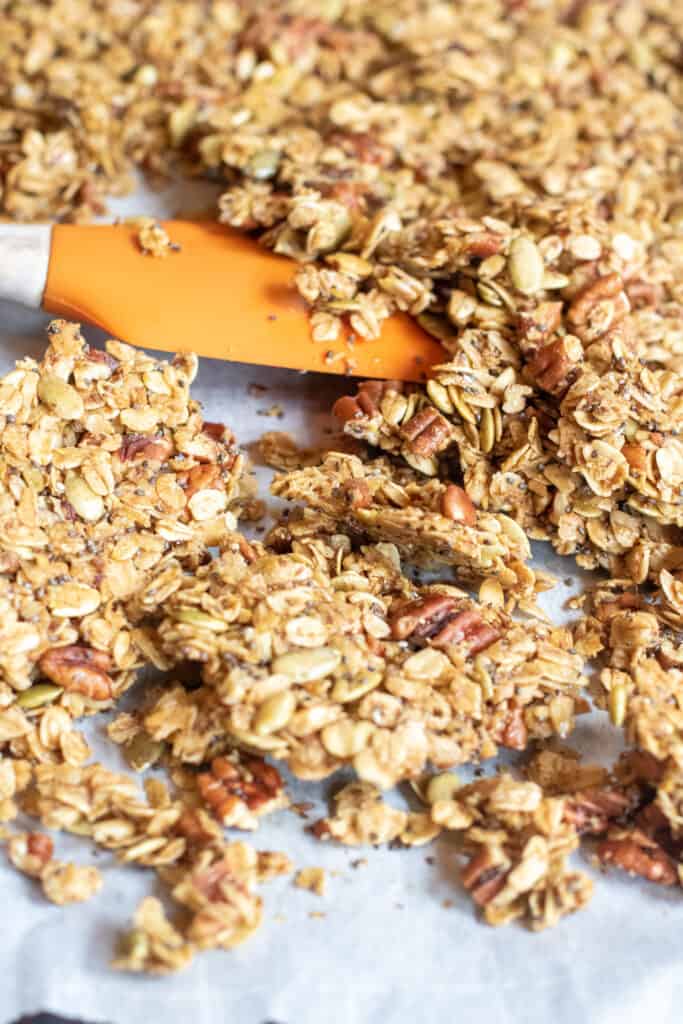 a close up of baked granola with a spatula breaking it into clusters 