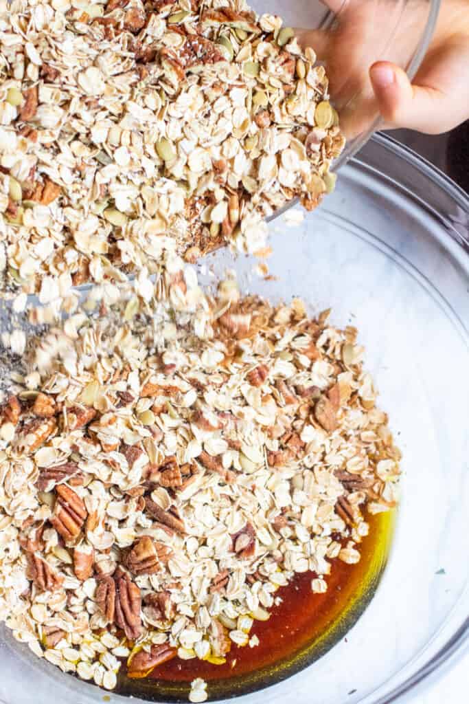 oat nut mixture being poured into bowl with maple syrup 