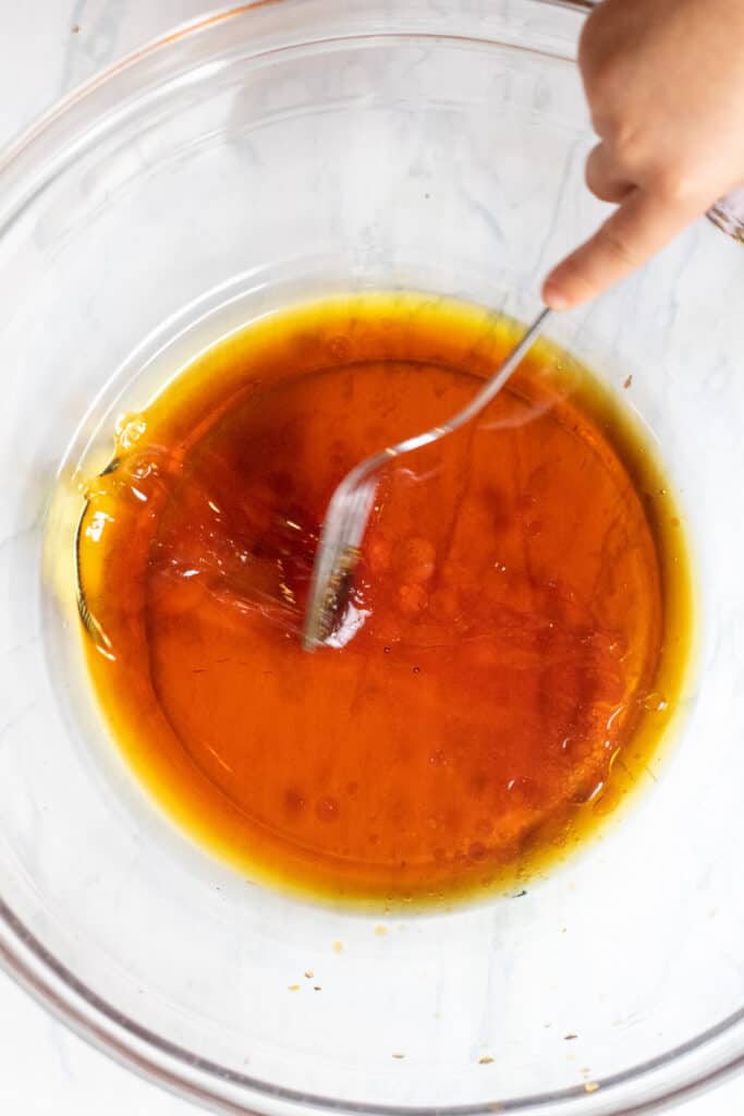 a bowl with maple syrup and oil and a fork being whisked 