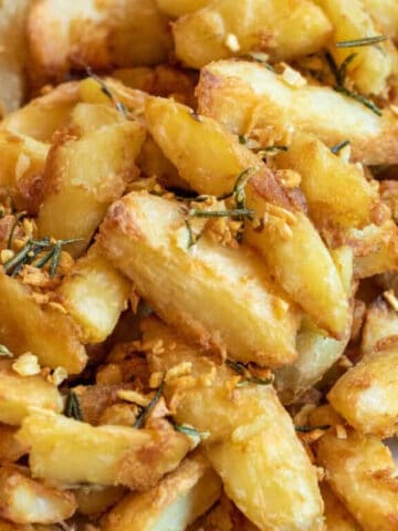 a plate of baked potato wedges topped with rosemary and garlic.