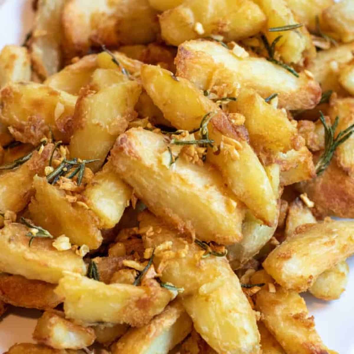 a plate of baked potato wedges topped with rosemary and garlic.