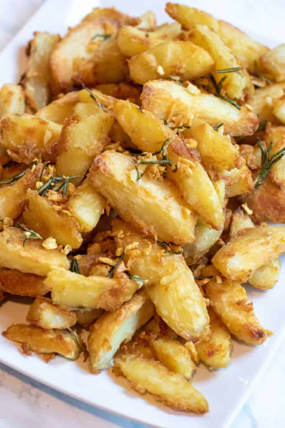 a plate of baked potato wedges topped with rosemary and garlic.
