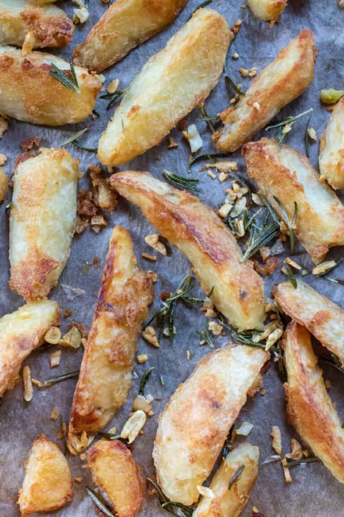 baked potato wedges on a baking sheet topped with garlic and rosemary.