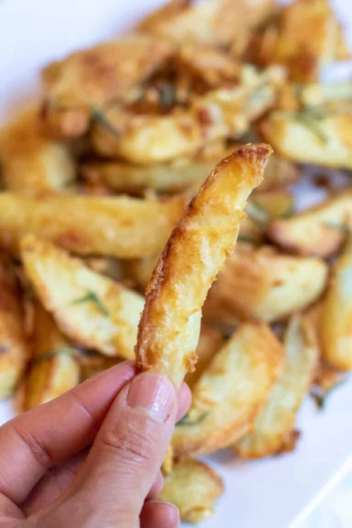 a hand holing up a crispy potato wedge.