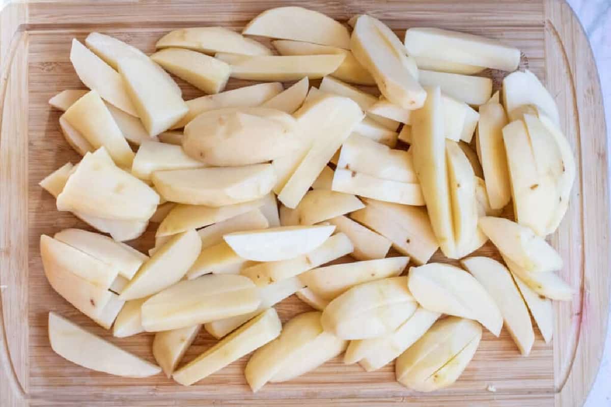 a cutting board with raw potatoes sliced.