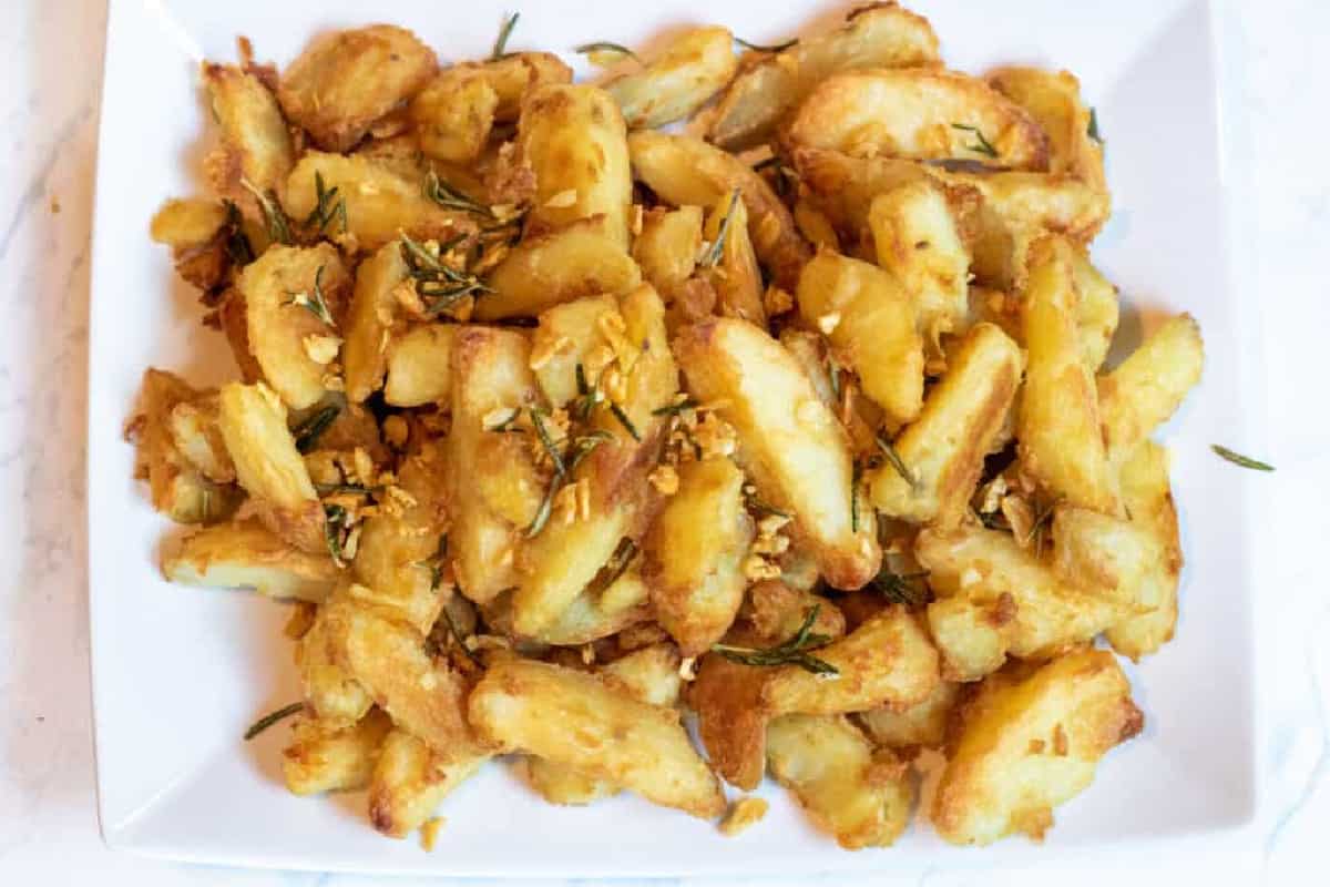 a plate of baked potato wedges topped with rosemary and garlic.