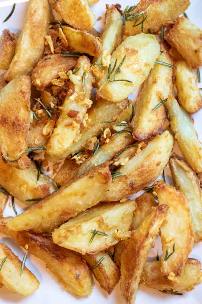 a plate of baked potato wedges topped with rosemary and garlic