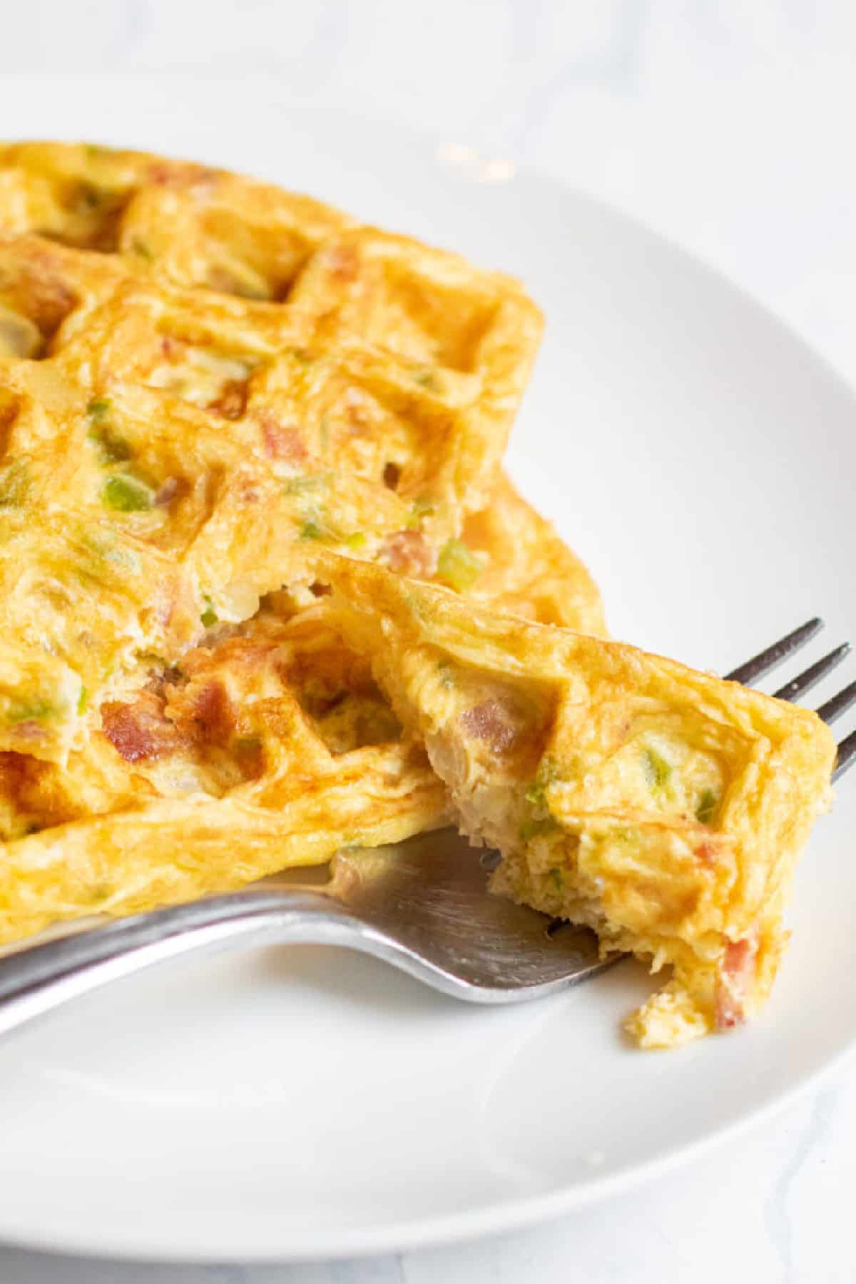 a plate with a fork taking a bite of egg waffle.