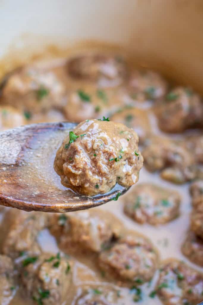 a wooden spoon holding up a  meatball over a pot 
