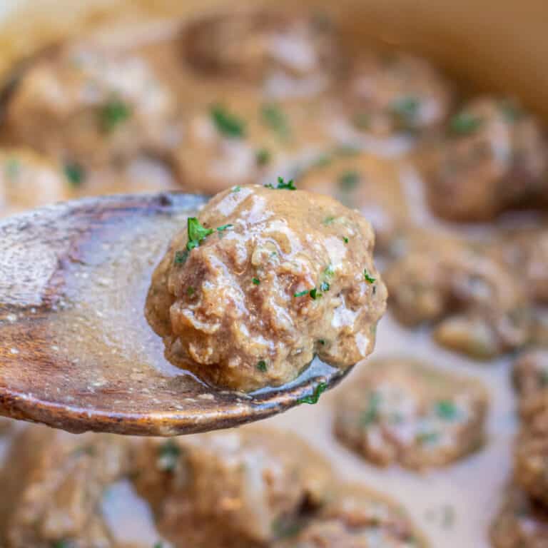 a wooden spoon holding up a swedish meatball over a pot of meatballs.
