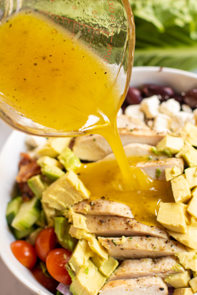 lemon vinaigrette being poured on a salad with chicken.