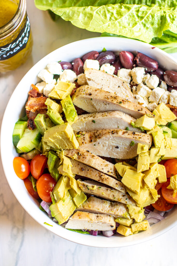 an over head of salad with chicken avocado, feta, olives, cucumbers, and tomatoes.