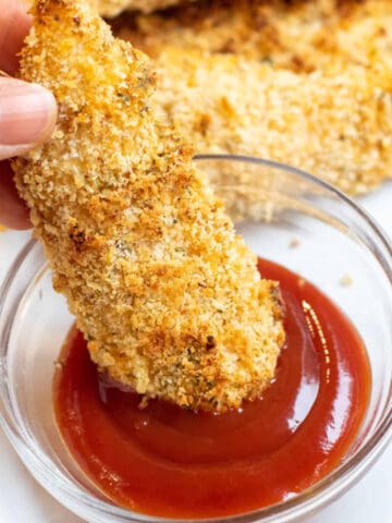 chicken tender being dipped in ketchup.