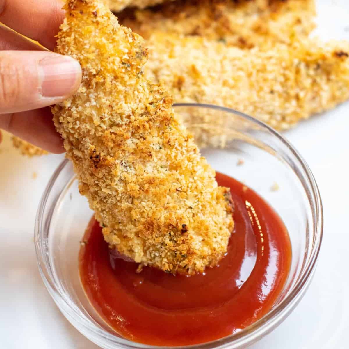 chicken tender being dipped in ketchup.