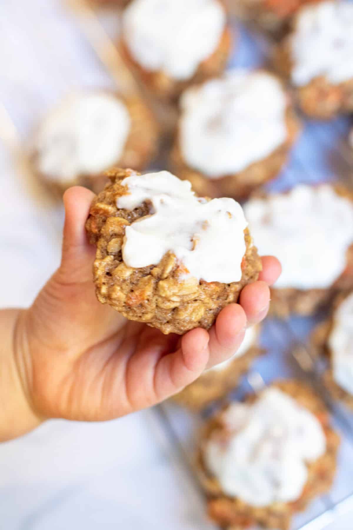 a toddler hand holding a frosted oatmeal cookie