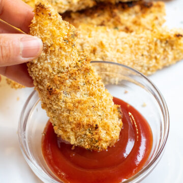 chicken tender being dipped in ketchup.