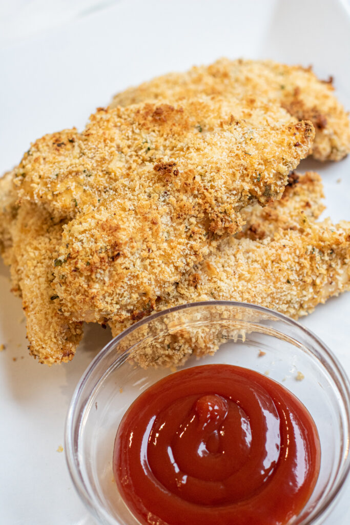 a plate of baked chicken tenders with some ketchup