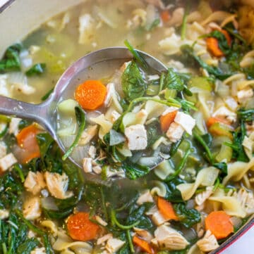 a pot of veggie noodle soup with spinach with ladle.