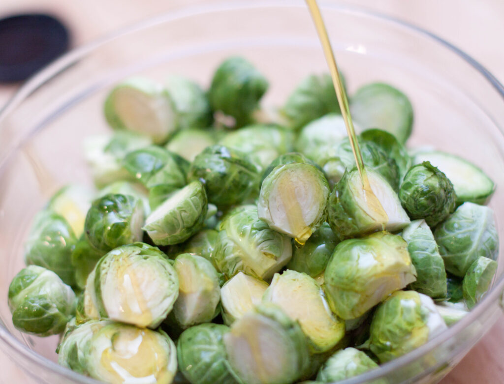 a bowl of brussels sprouts with oil being poured in.
