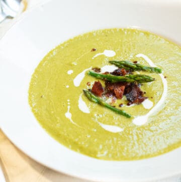 a close up of a bowl of creamy green soup with asparagus and bacon on top.