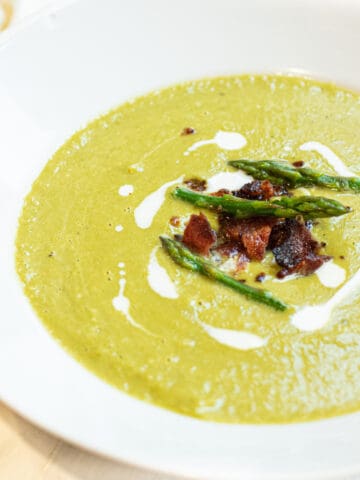 a close up of a bowl of creamy green soup with asparagus and bacon on top.