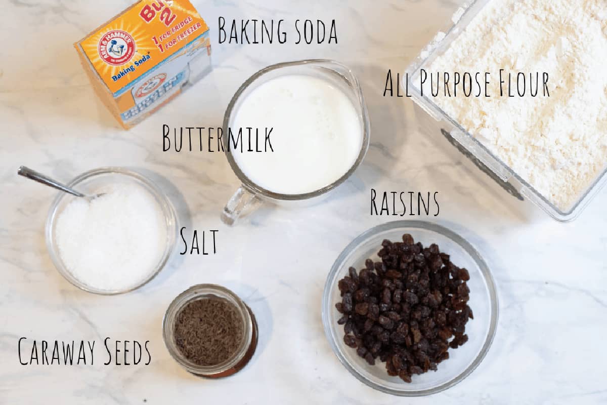 flour, raisins, baking soda, buttermilk, caraway seeds, and salt on a counter.