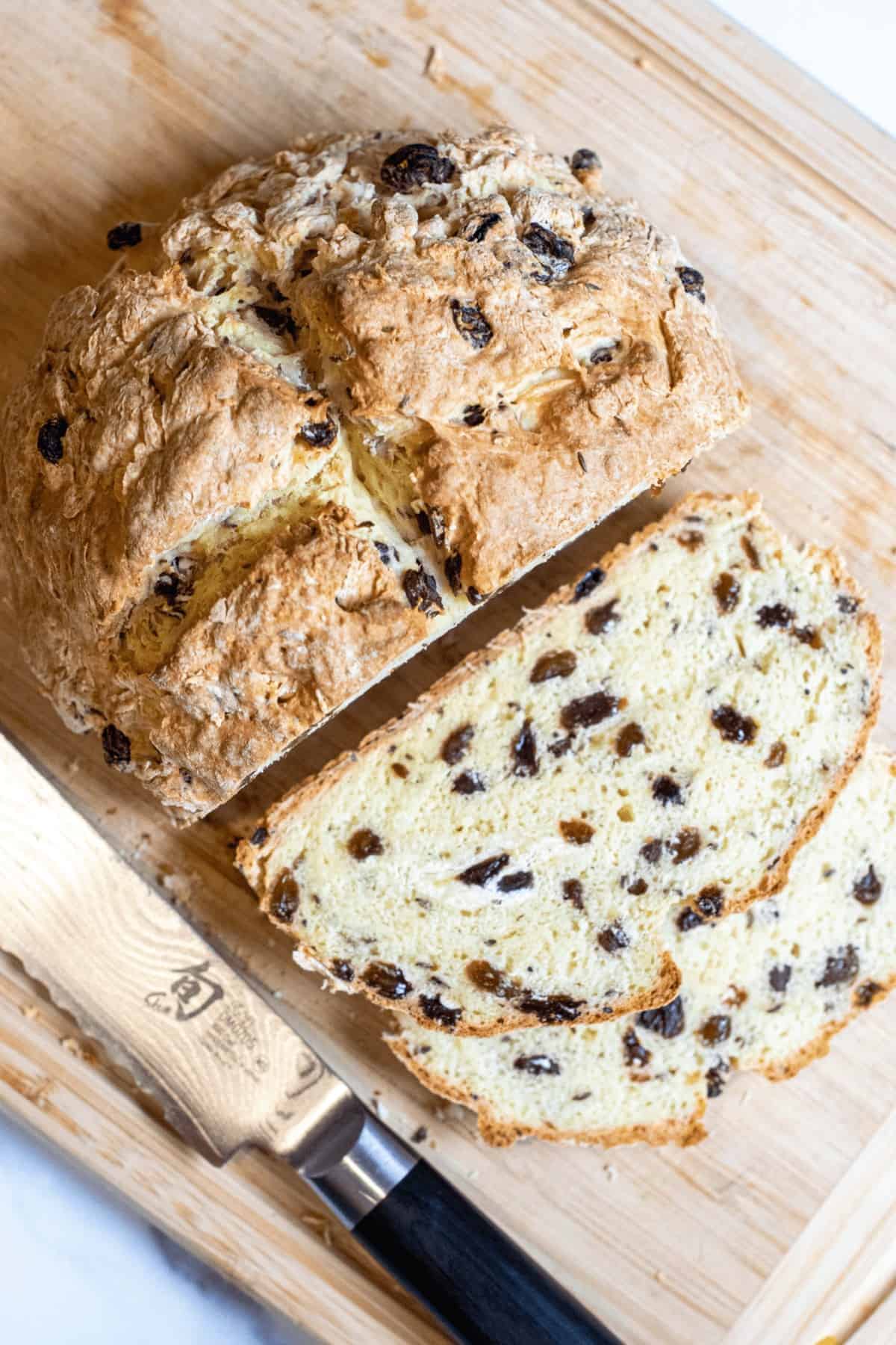 sliced soda bread with raisins on a cutting board with a knife.