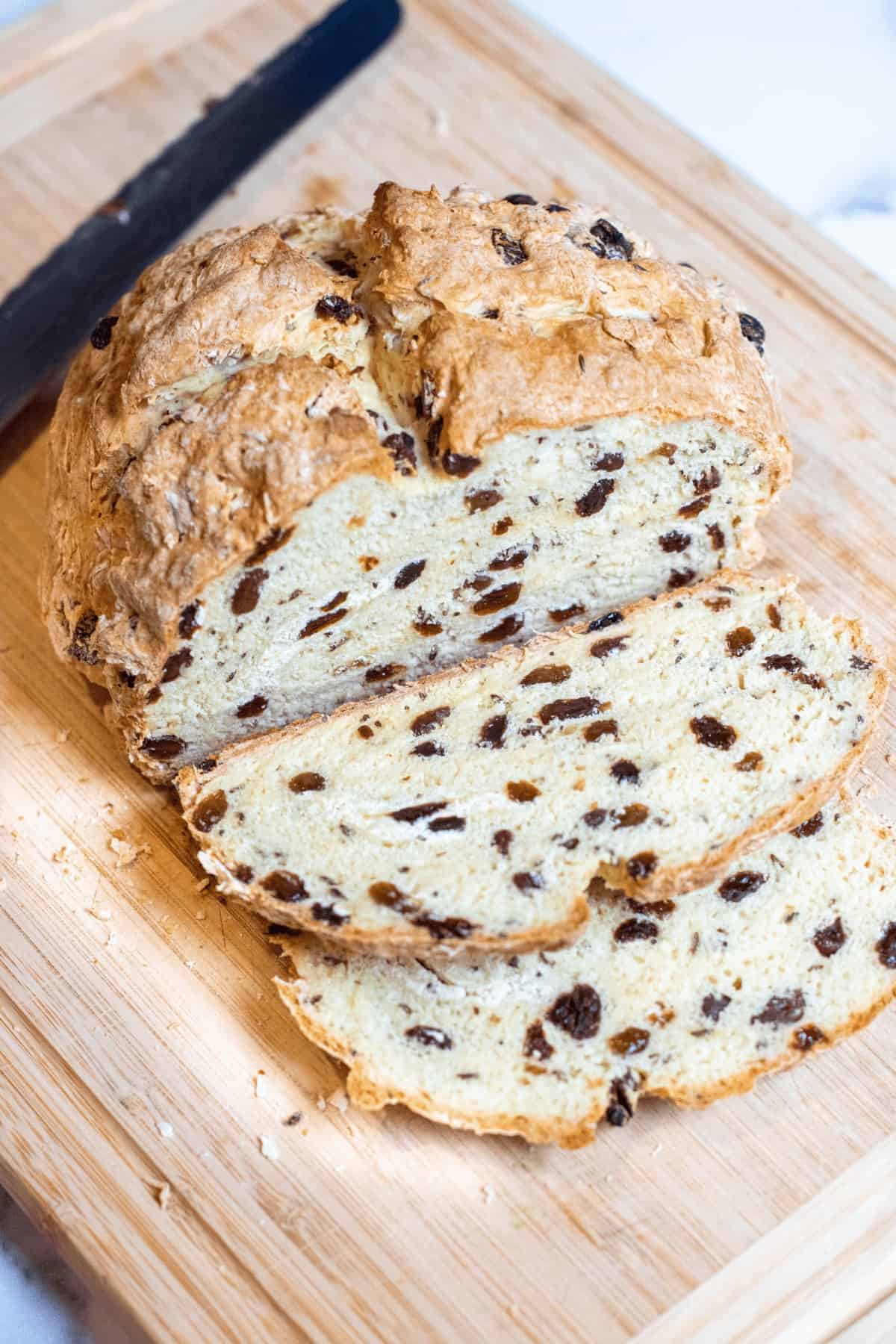 sliced soda bread with raisins on a cutting board with a knife.