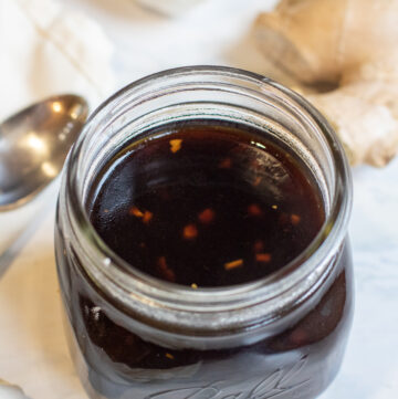 a jar of brown sauce with a spoon ginger, and garlic next to it.