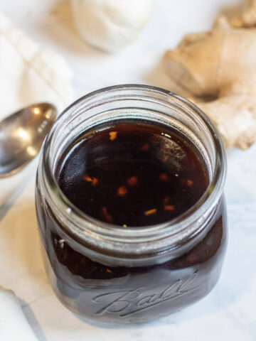 a jar of brown sauce with a spoon ginger, and garlic next to it.