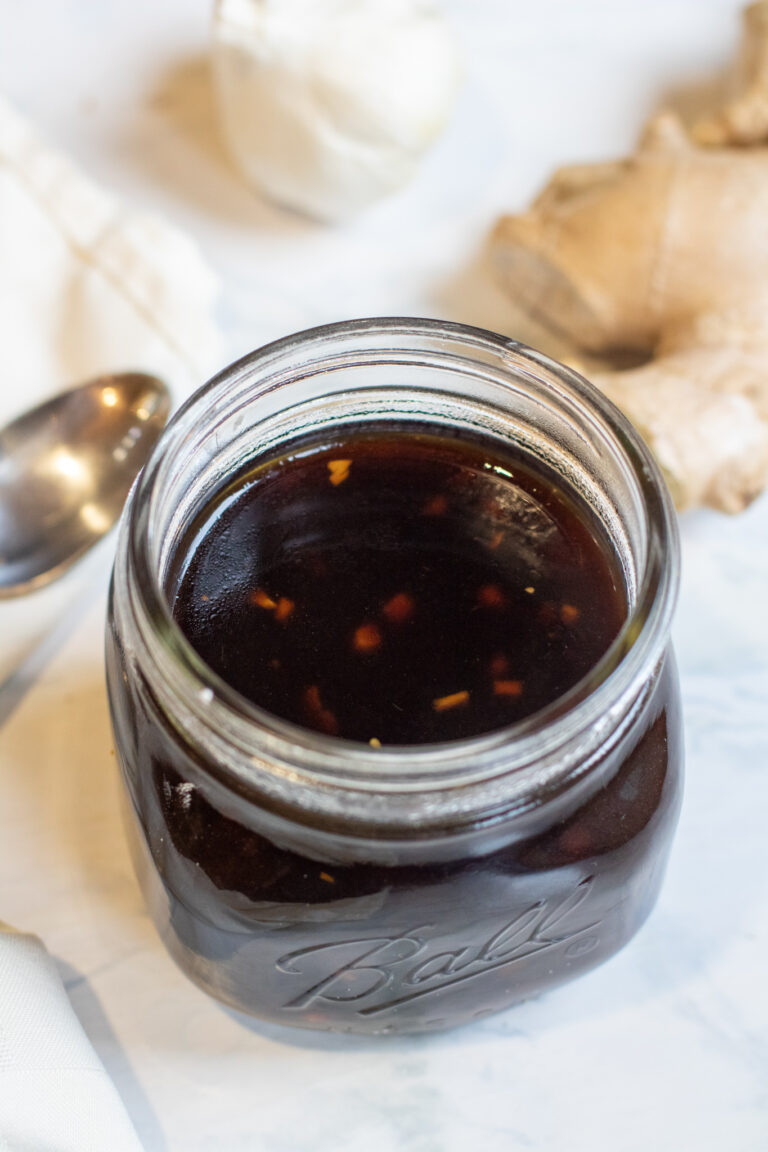 a jar of brown sauce with a spoon ginger, and garlic next to it.