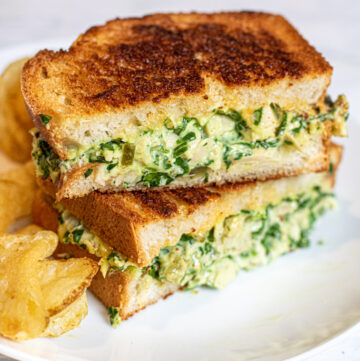 stacked tuna melt with spinach on a plate with chips.